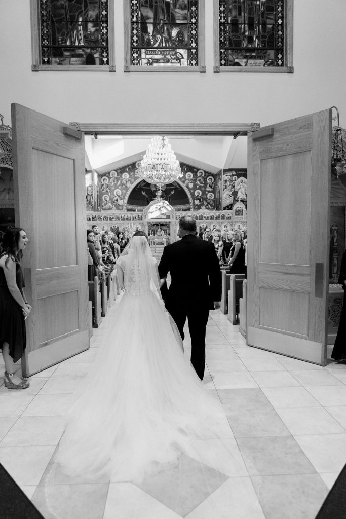 The back of the bride entering into the church with her father black and white photograph