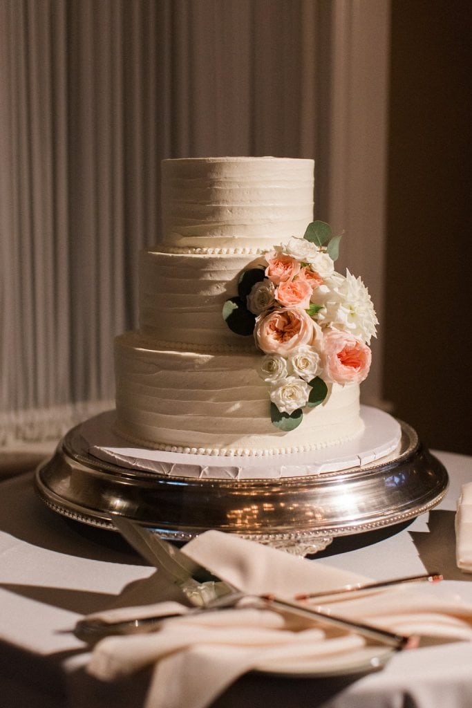 Wedding cake decorated with pink and white flowers during the reception