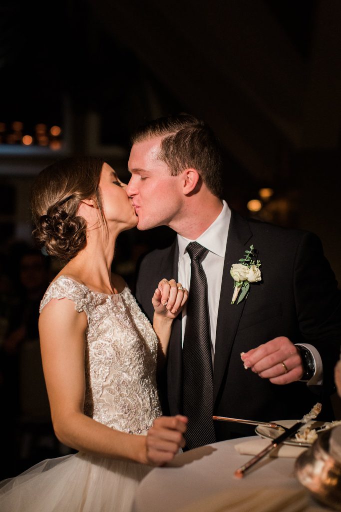 The bride and groom cutting their wedding cake and sharing a kiss at their reception