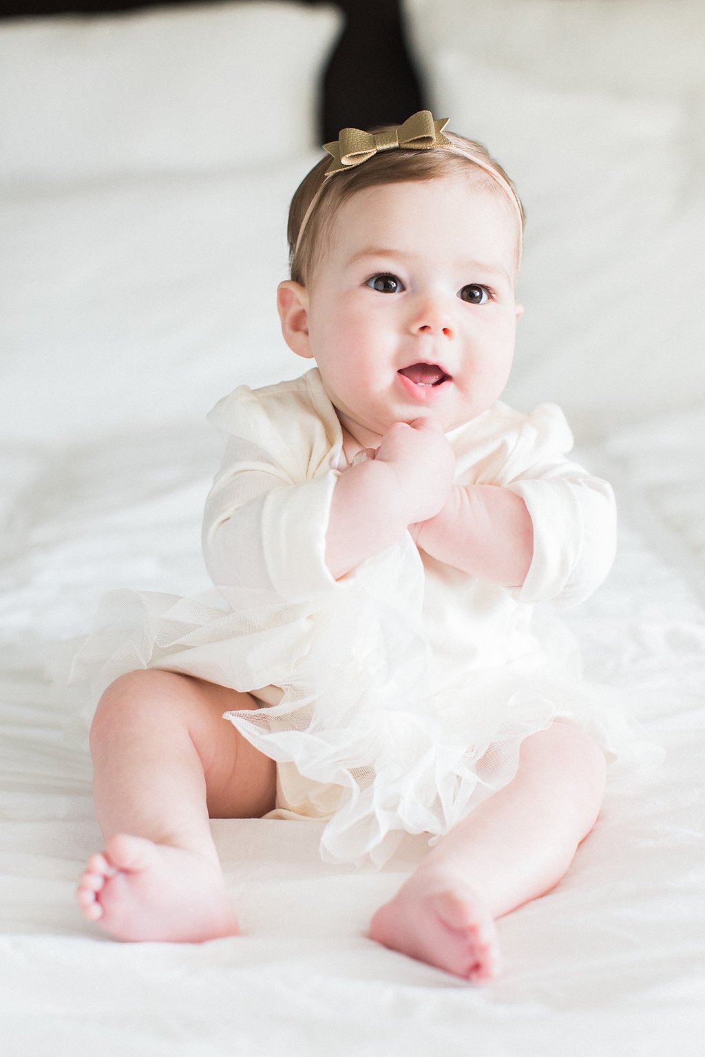 Lifestyle Photography - Lauren Renee Photography Baby clapping her hands and posing in a white dress with gold bow in her hair