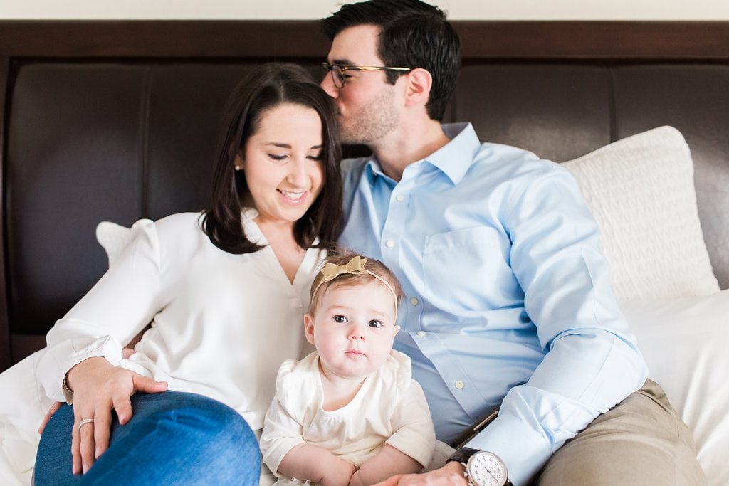 Dad kissing mom on the head while baby looks at camera during in home lifestyle family photos
