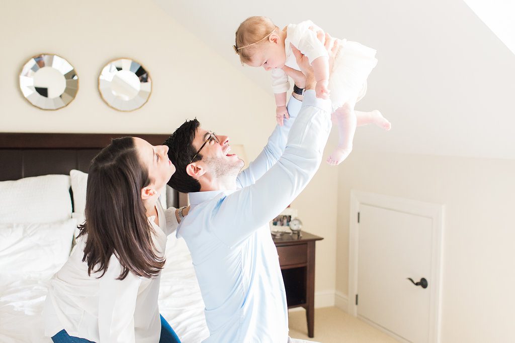 Dad holding baby in the air and mom smiling in their bedroom for family portraits