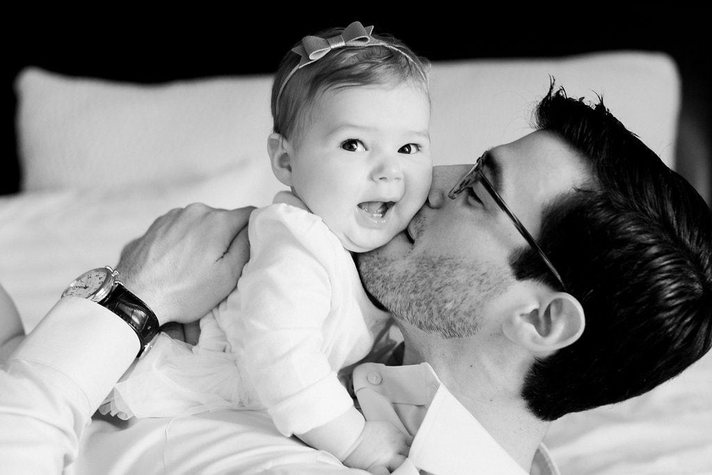 Dad kissing his daughter on the cheek and baby smiles during in home family photos black and white