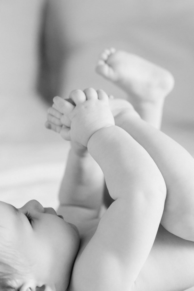 Naked baby grabbing at her feet in a black and white portrait