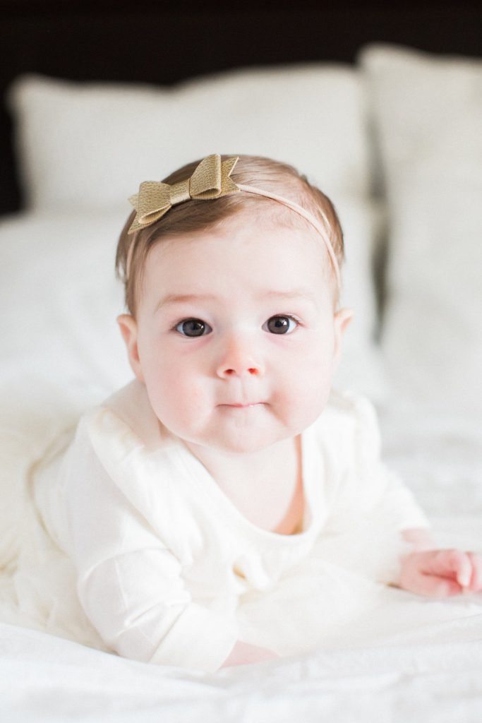 Portrait of baby on a bed in white dress with gold bow