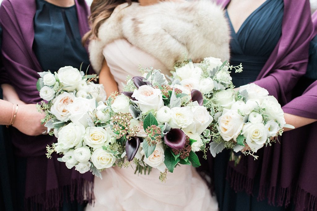 close up photo of bride with bridesmaids and bouquets of white and purple flowers