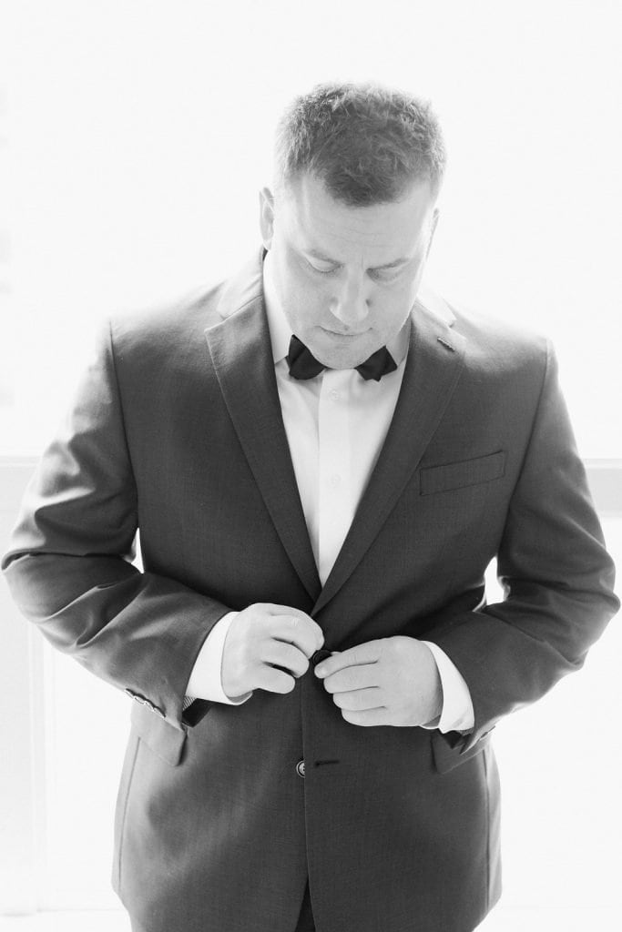 Groom buttoning up and getting dressed in his suit at the hotel