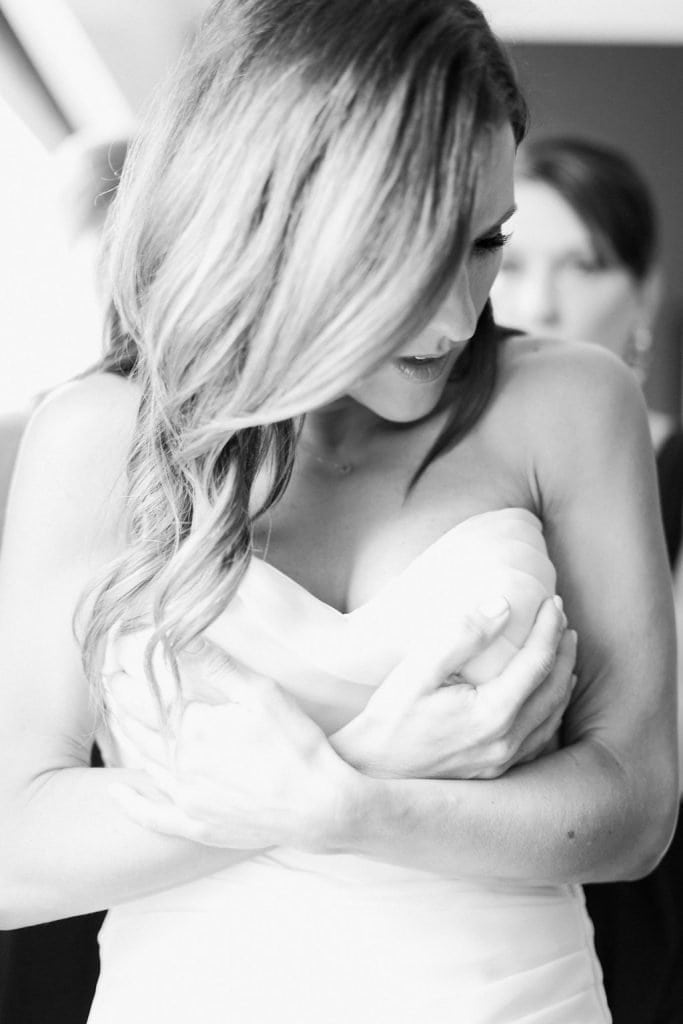 Bride getting zipped into her dress in black and white photo