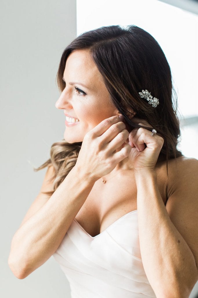 Photograph of the bride putting on her jewelry and earrings while getting ready
