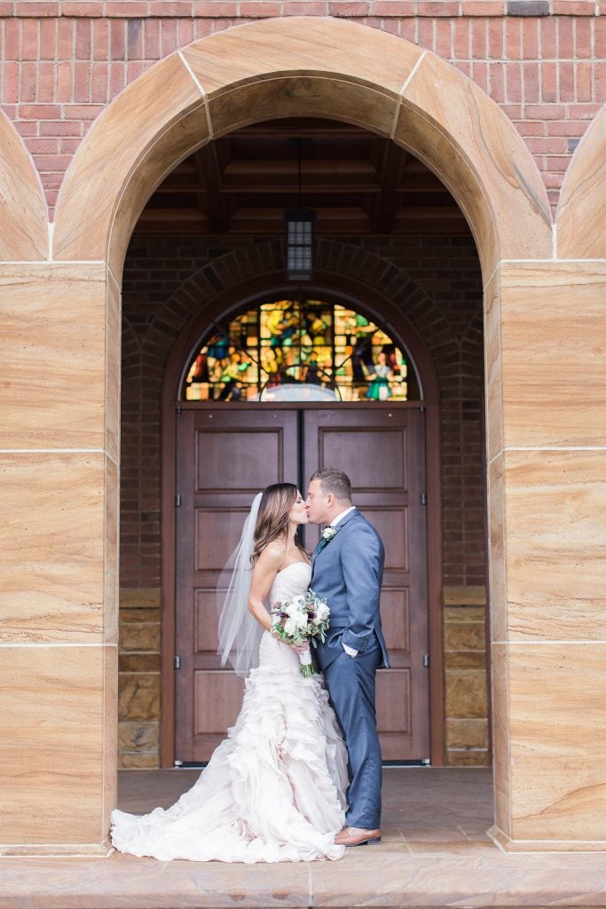 Photograph of the bride and groom kissing in the archway outside Saints John and Paul Roman Catholic Church