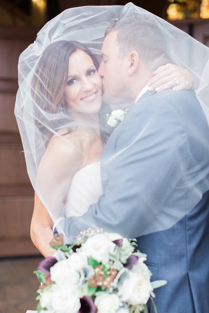 Photo of the groom kissing the bride's cheek under her veil outside the church