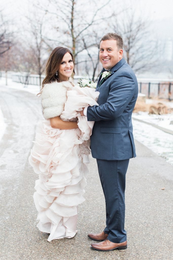 Portrait of the groom holding the bride's dress in the snow during their Pittsburgh winter wedding at J. Verno Studios