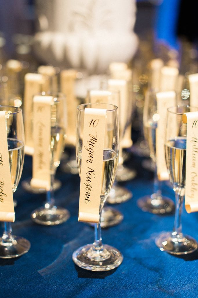 Calligraphy escort scrolls sitting in glasses of champagne for guests at this winter wedding