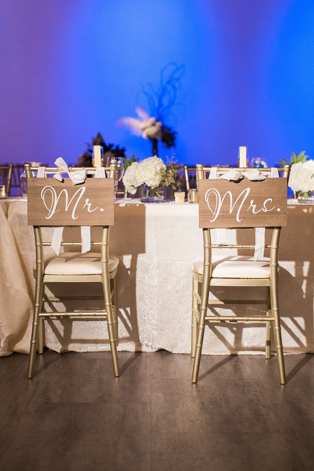 Pittsburgh Wedding Photography - Lauren Renee Photography Calligraphy Mr. and Mrs. on wood signs over the back of gold chiarvari chairs with blue uplighting