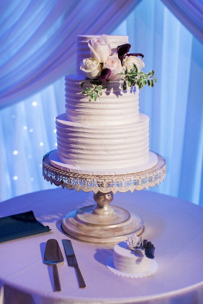 Simple white wedding cake with blush pink and purple accent flowers from Oakmont Bakery