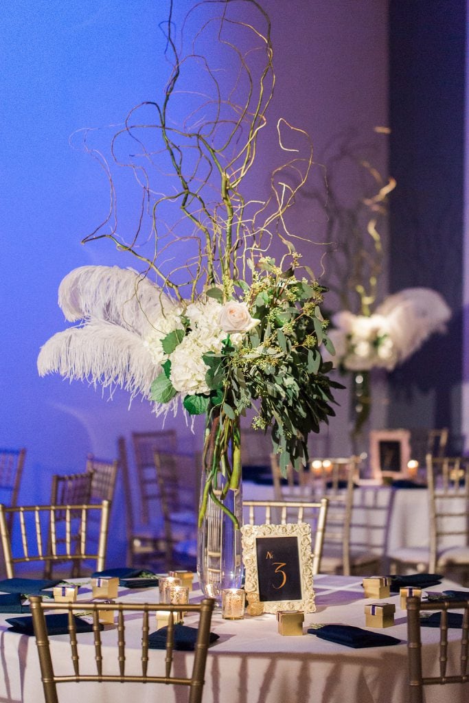 Tall floral centerpieces with white feathers and flowers at winter wedding reception