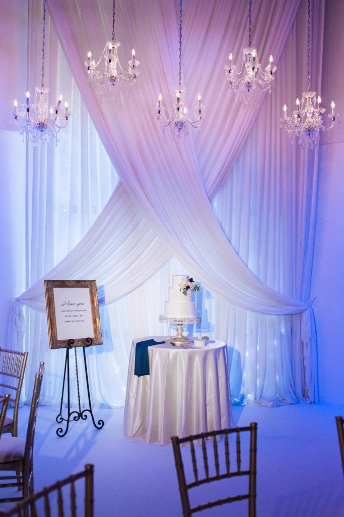 Wedding cake under chandeliers at reception at J. Verno Studios