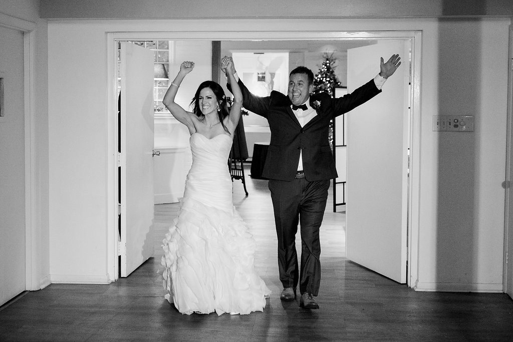 Bride and groom enter into their wedding reception holding hands in a black and white photo