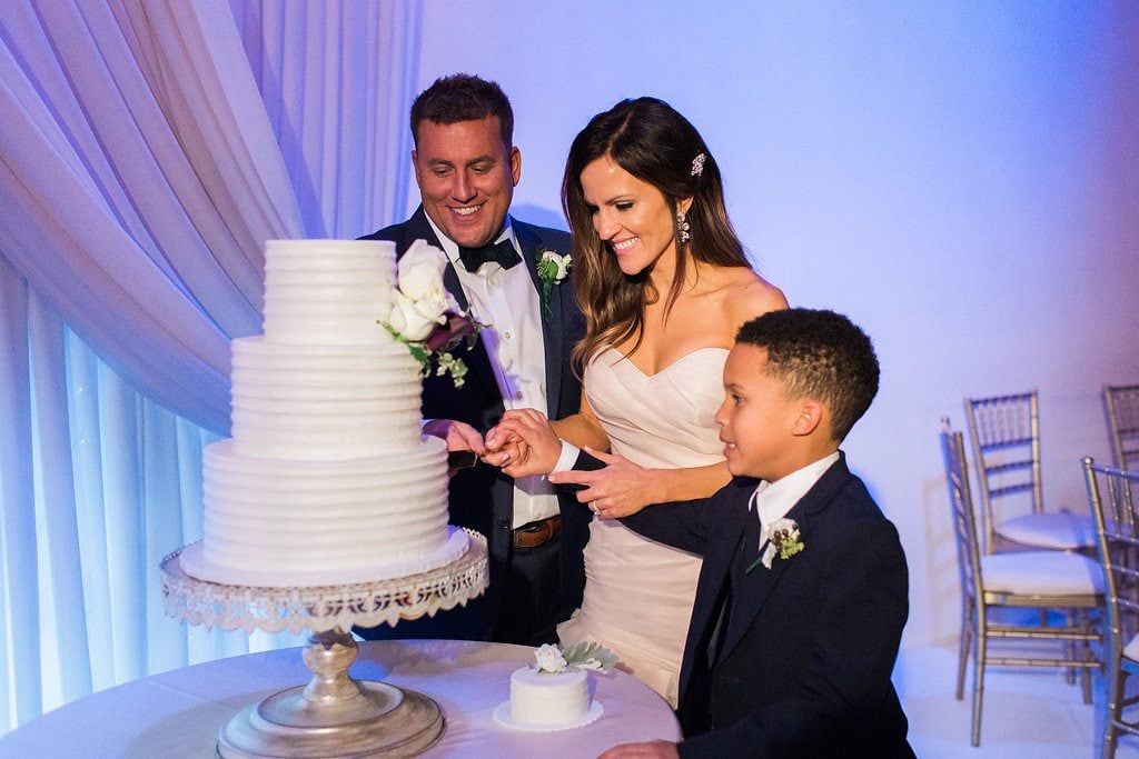 Bride and Groom cutting their white three tiered cake during their wedding reception at J. Verno Studios