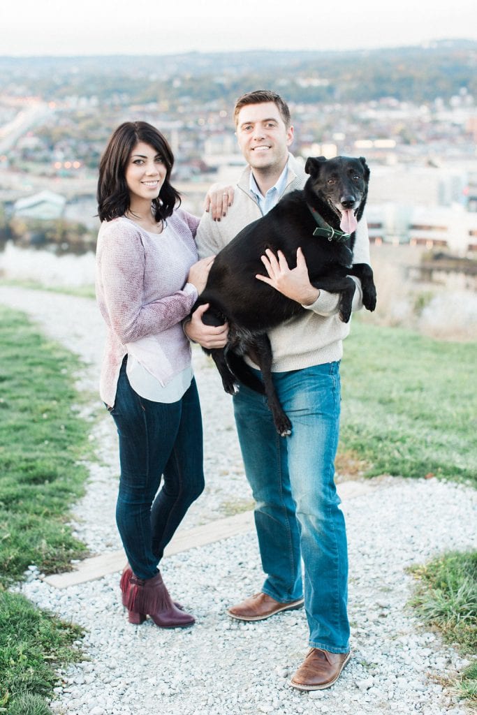Mount Washington and South Side Engagement Couple posing with their dog in a photo on top of Mount Washington overlooking Pittsburgh