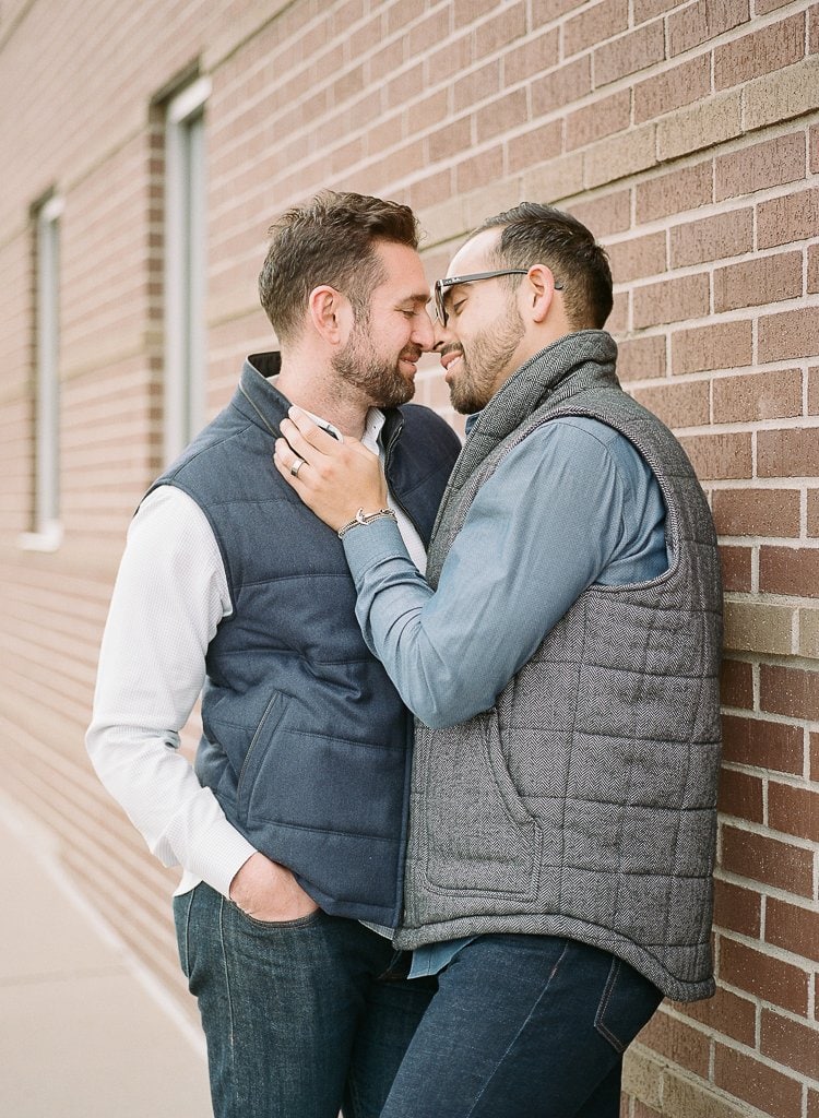 Sam-Sex Engagement Session - Lauren Renee Photography two gay men embracing leaning against a brick wall in downtown Denver Colorado