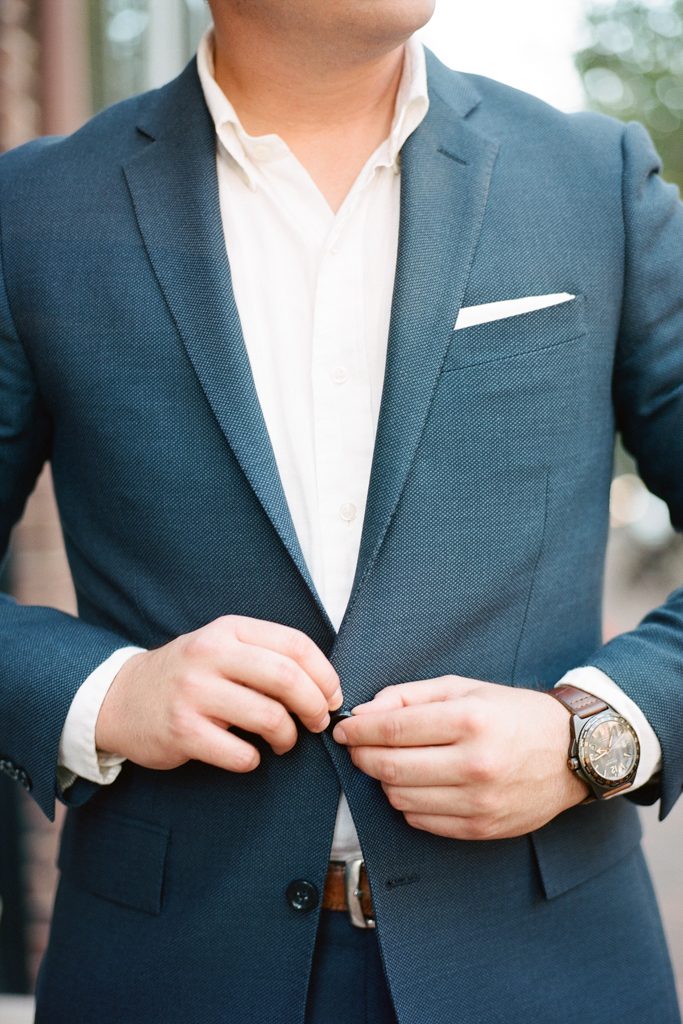 groom buttoning up his blue suit during engagement photos