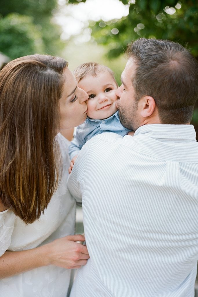 Mom and Dad snuggling their baby and kissing him on the cheeks