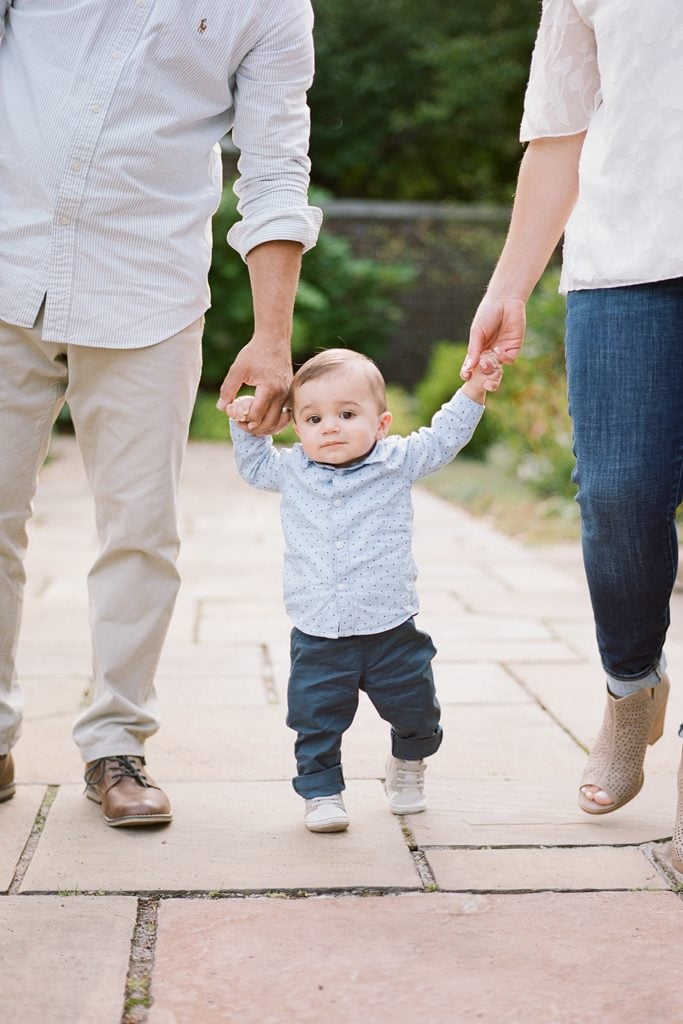 Mom and Dad holding their baby son's hands while he learned to walk