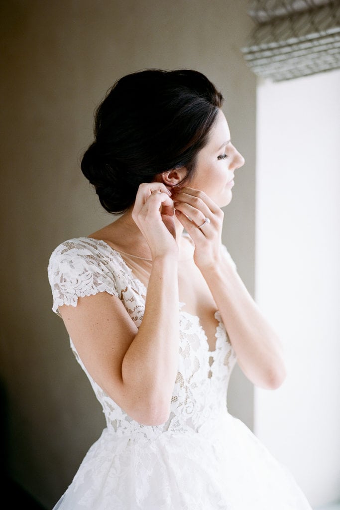 Bride putting on her earrings while getting ready for her wedding day