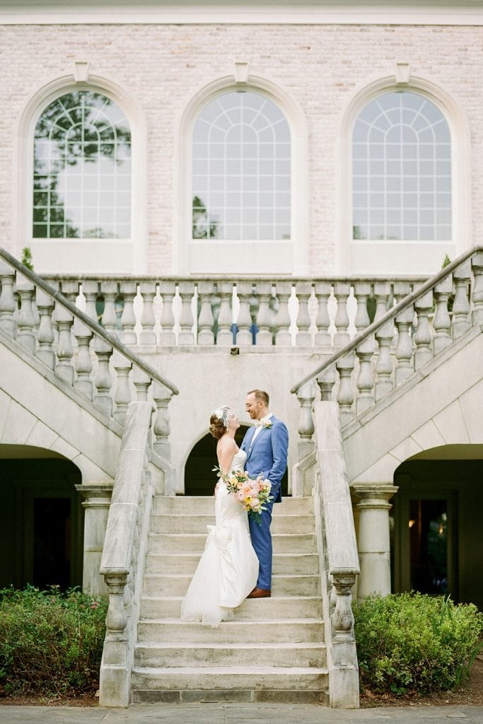 bride and groom standing on staircase in front of mansion with arch windows