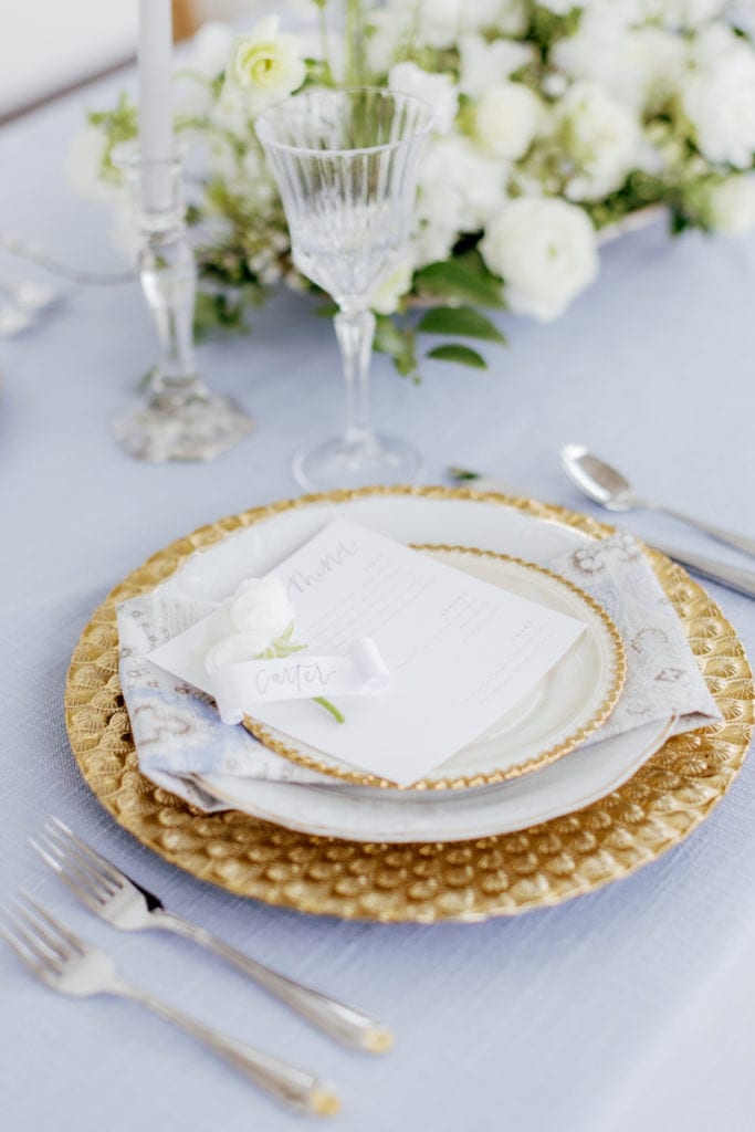 Wedding table top decor with blue linen and gold accented dishes and silverware