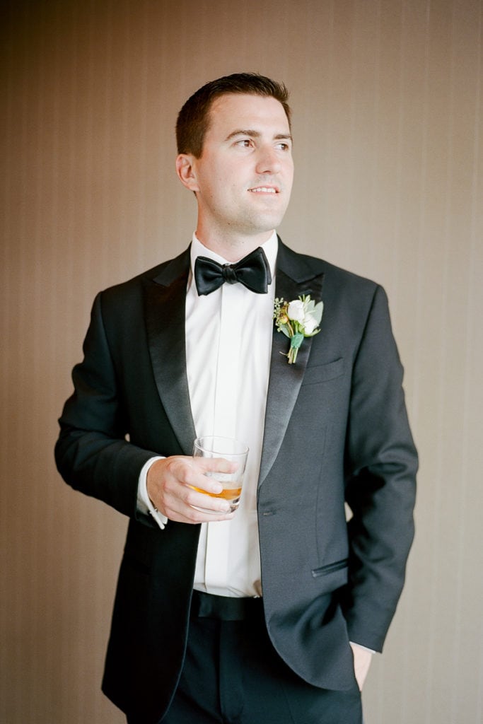 Groom holding a glass of whiskey while getting ready for his wedding