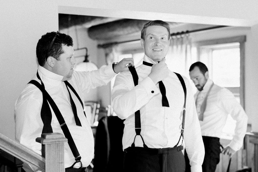 Groomsmen helping the groom get ready and tie his bowtie