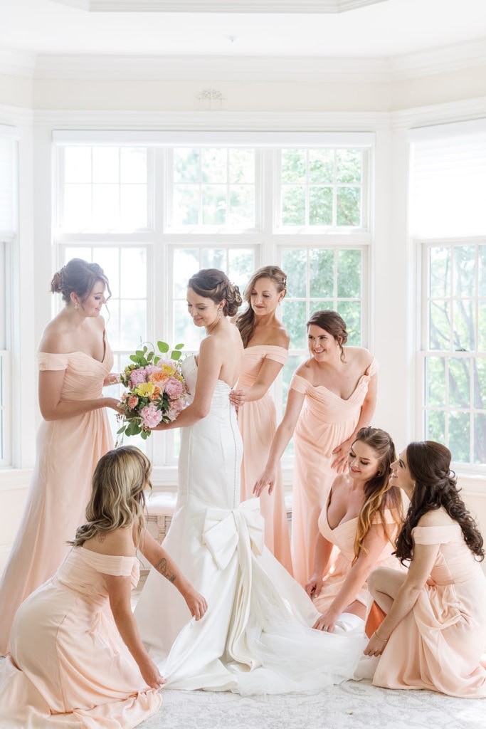 Bridesmaids in pink dresses helping with bride's bow wedding dress