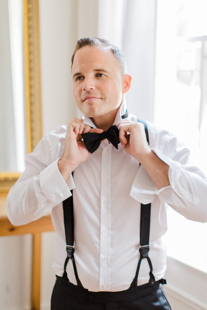 Groom putting on tuxedo bow tie