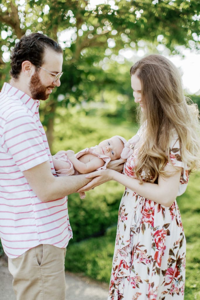 parents holding their newborn in between them in an english garden: outdoor newborn session