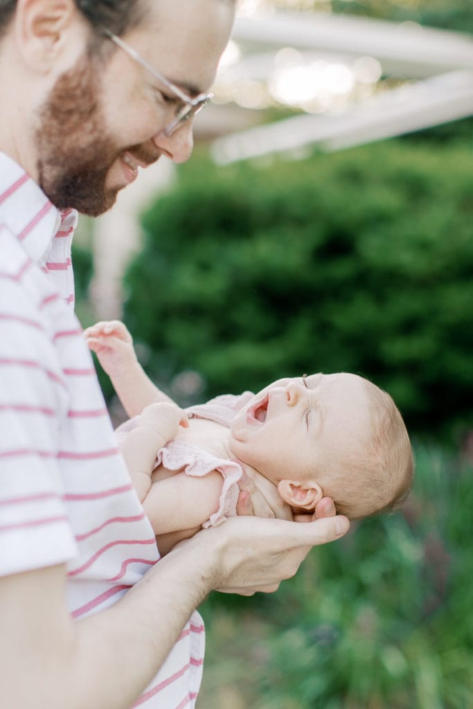 Newborn baby girl being held by her dad while she yawns: outdoor newborn session