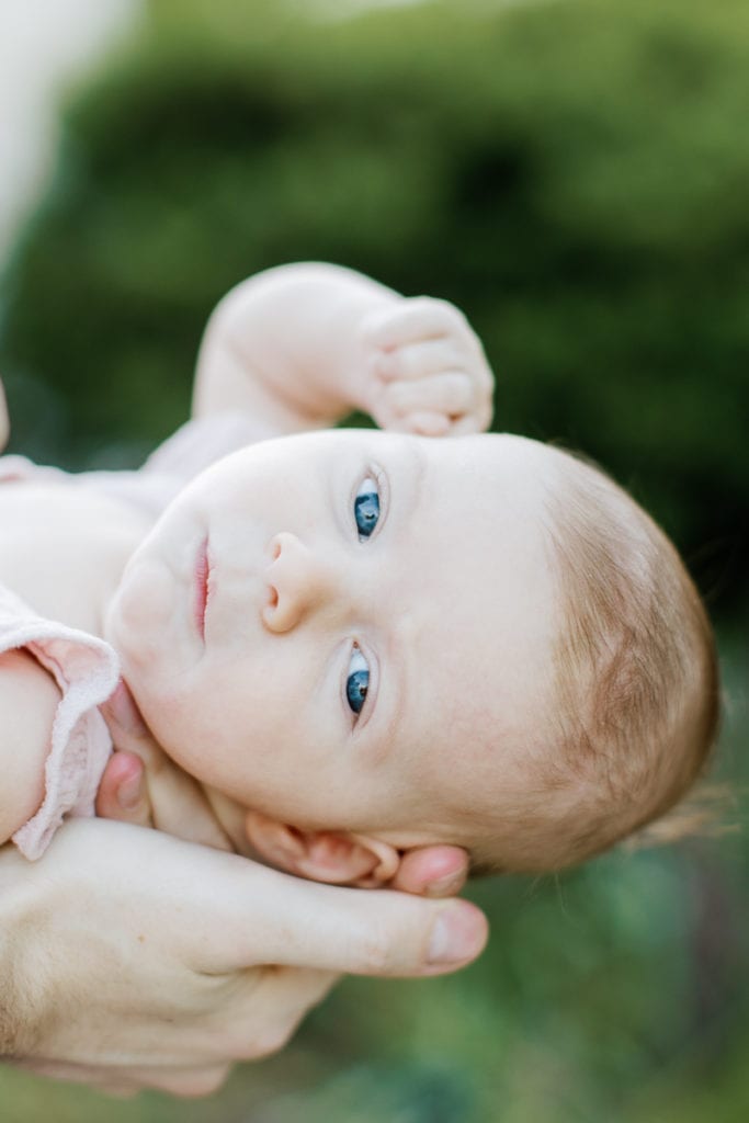 newborn baby girl with bright blue eyes wearing a pink romper: outdoor newborn session