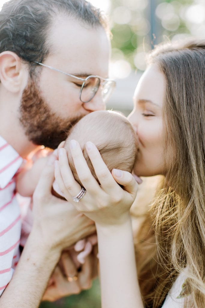 parents holding their newborn baby in between themselves while kissing her head: outdoor newborn session