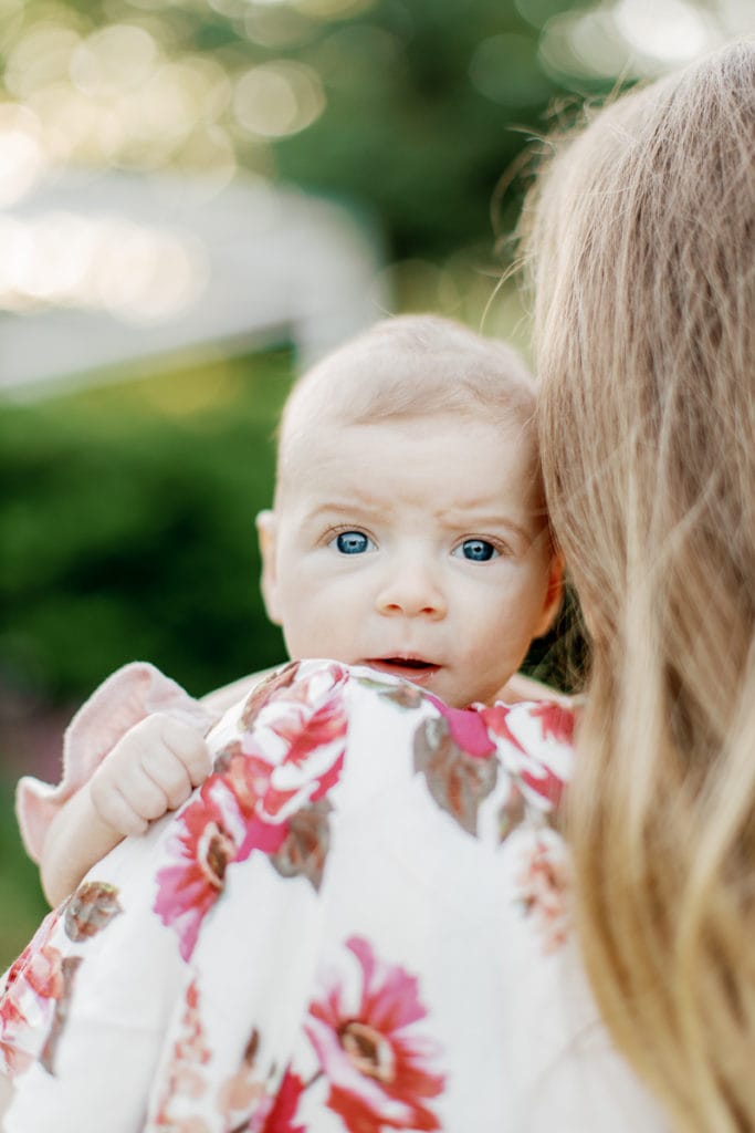 newborn baby with blue eyes looking into the camera over mother's shoulder: outdoor newborn session