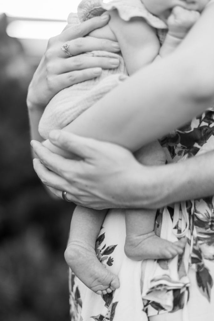 black and white photo of parents hands around their newborn baby: outdoor newborn session