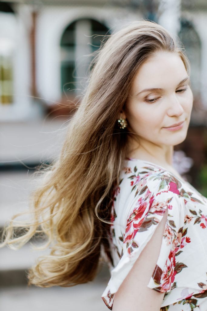 woman wearing pink floral dress with brown hair blowing in the breeze: outdoor newborn session