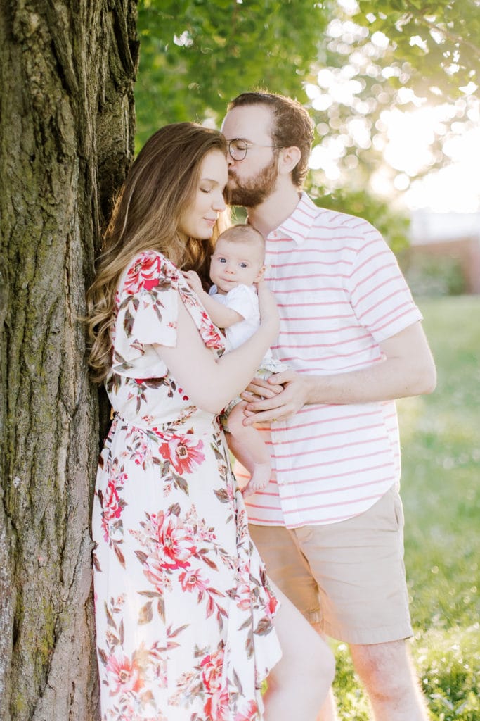 family hugging and holding their newborn baby leaning on a tree: outdoor newborn session