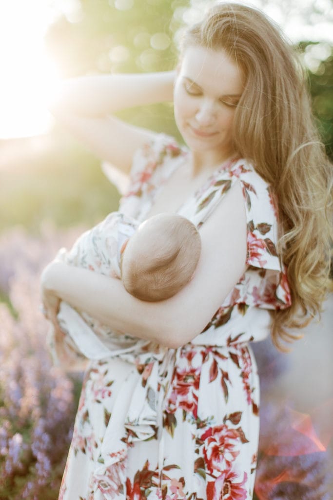 New mother holding her newborn while walking through lavender: outdoor newborn session