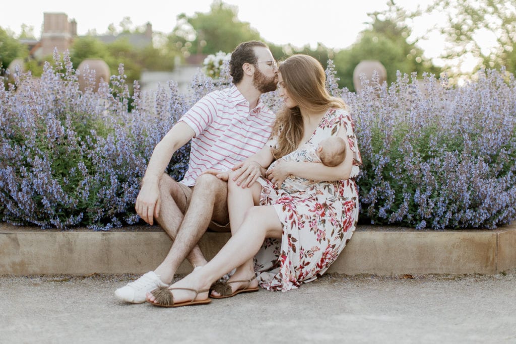 Man in pink and white striped shirt kissing woman holding newborn baby on the forehead: outdoor newborn session: outdoor newborn session
