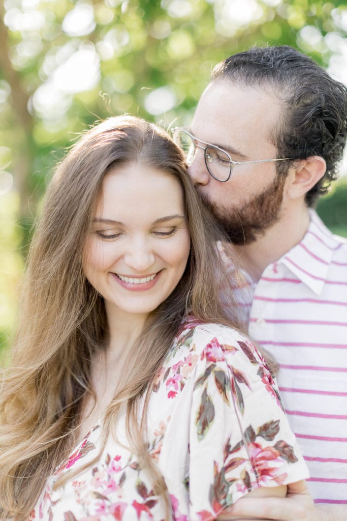 man kissing wife on the head while smiling and laughing: outdoor newborn session