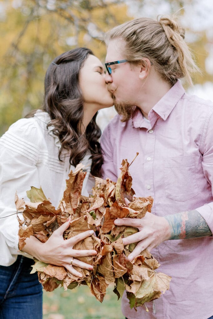 Husband and wife kissing while holding a bundle of fall leaves