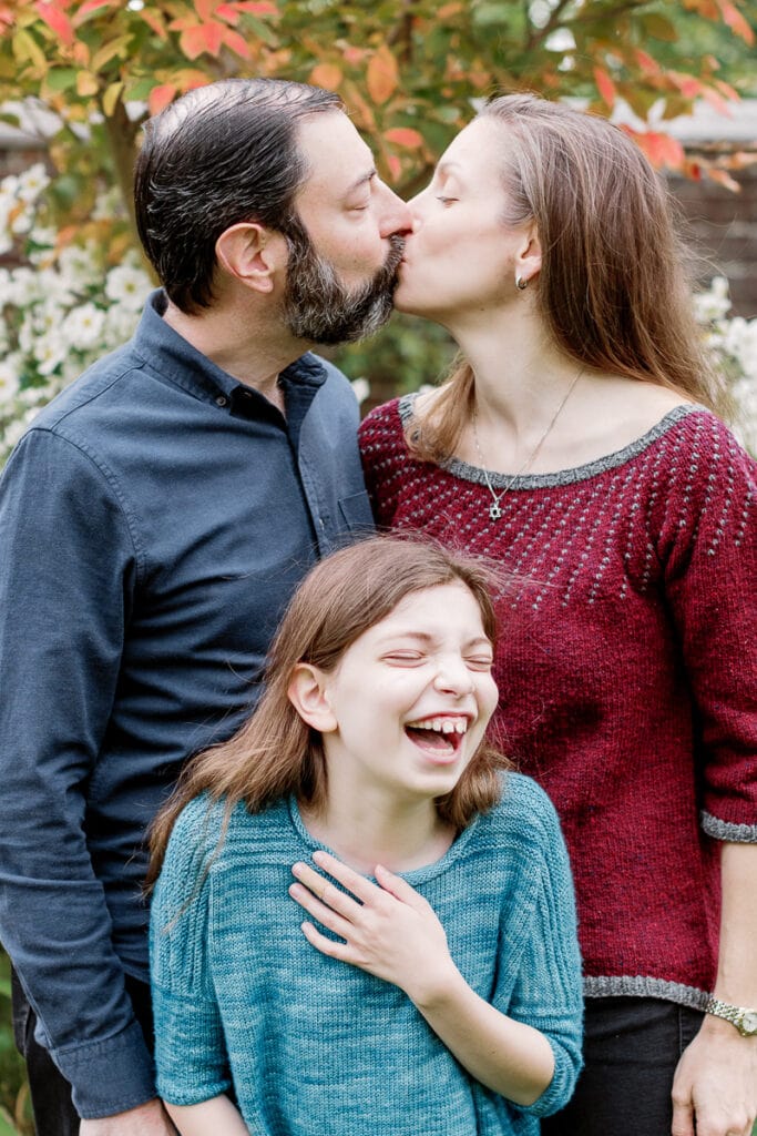 Little girl laughing as her parents kiss