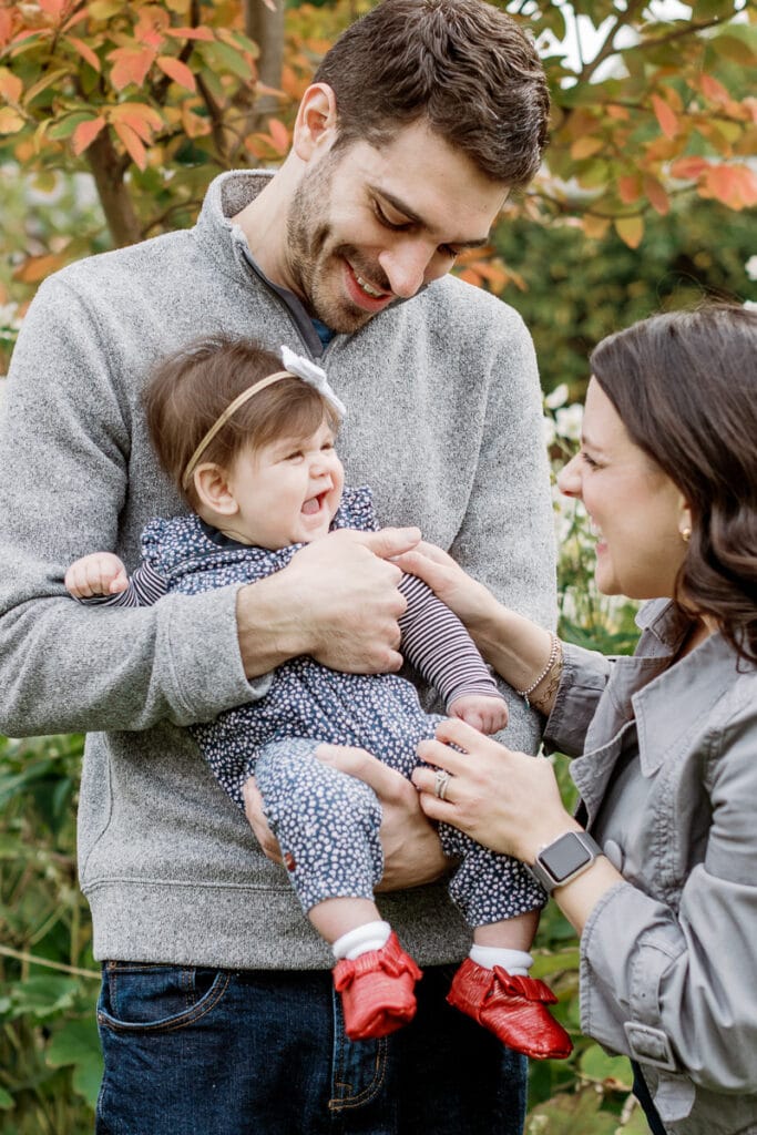 Dad holding baby girl while mom gets baby to smile