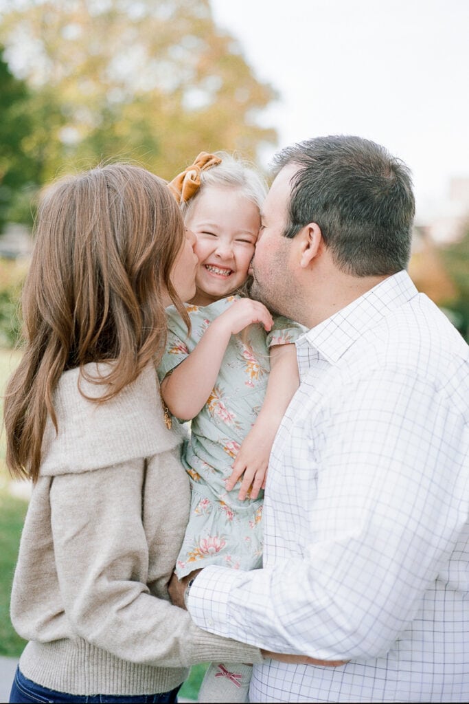 Mom and dad kissing daughter's cheeks